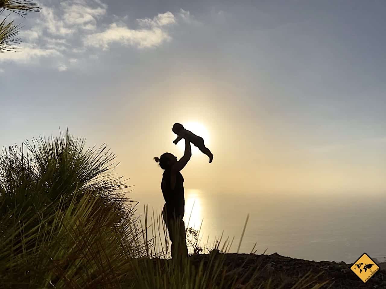 Silhouette einer Mutter mit Kind bei Sonnenuntergang gegen Himmel, Umrisse vor gelblichem Licht