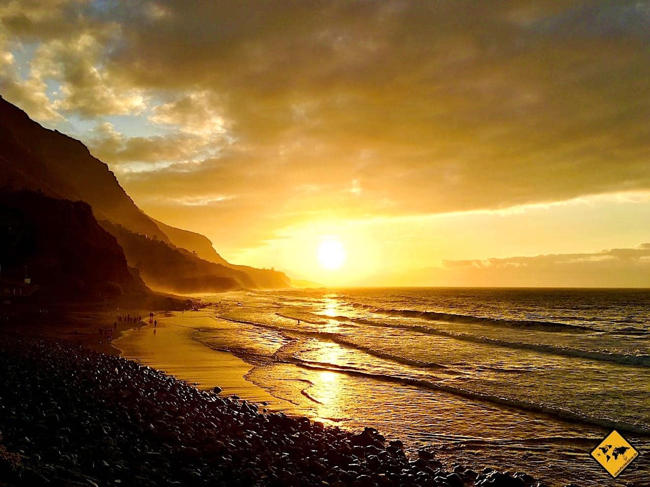 Sonnenuntergang über Strand mit Klippe, golden-orange gefärbtes Meer und Himmel
