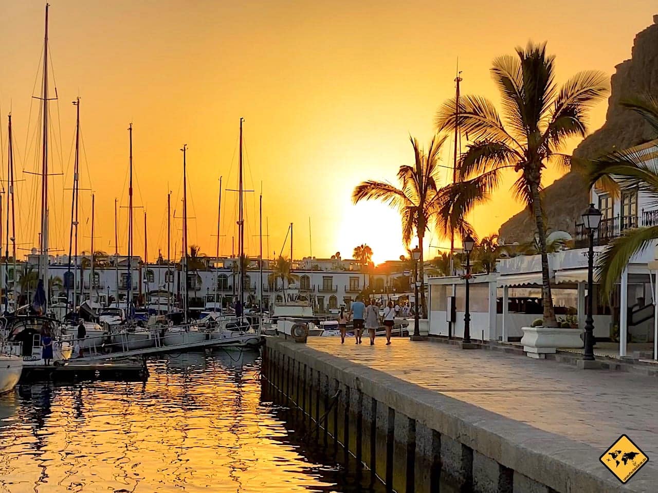 Hafen bei Sonnenuntergang mit Segelbooten, Palmen und Gebäuden am Wasser