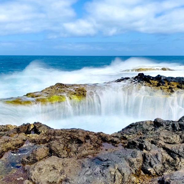 Langzeitbelichtung einer Welle an Felsen mit weicher Wassereffekt und blauem Himmel