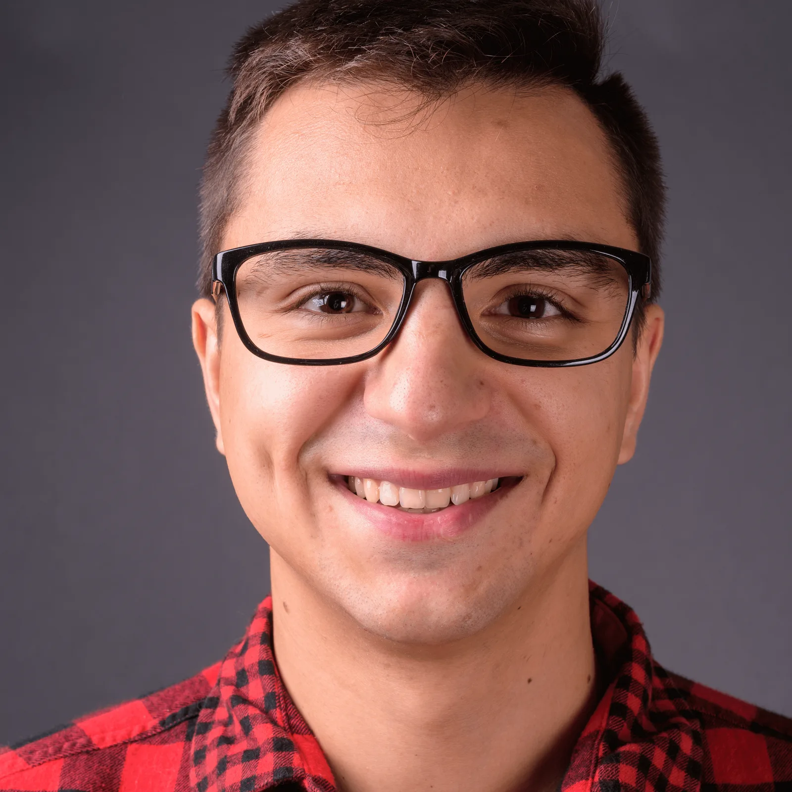 Porträt von Christoph mit Brille, rotes Karohemd, lächelnd vor grauem Hintergrund
