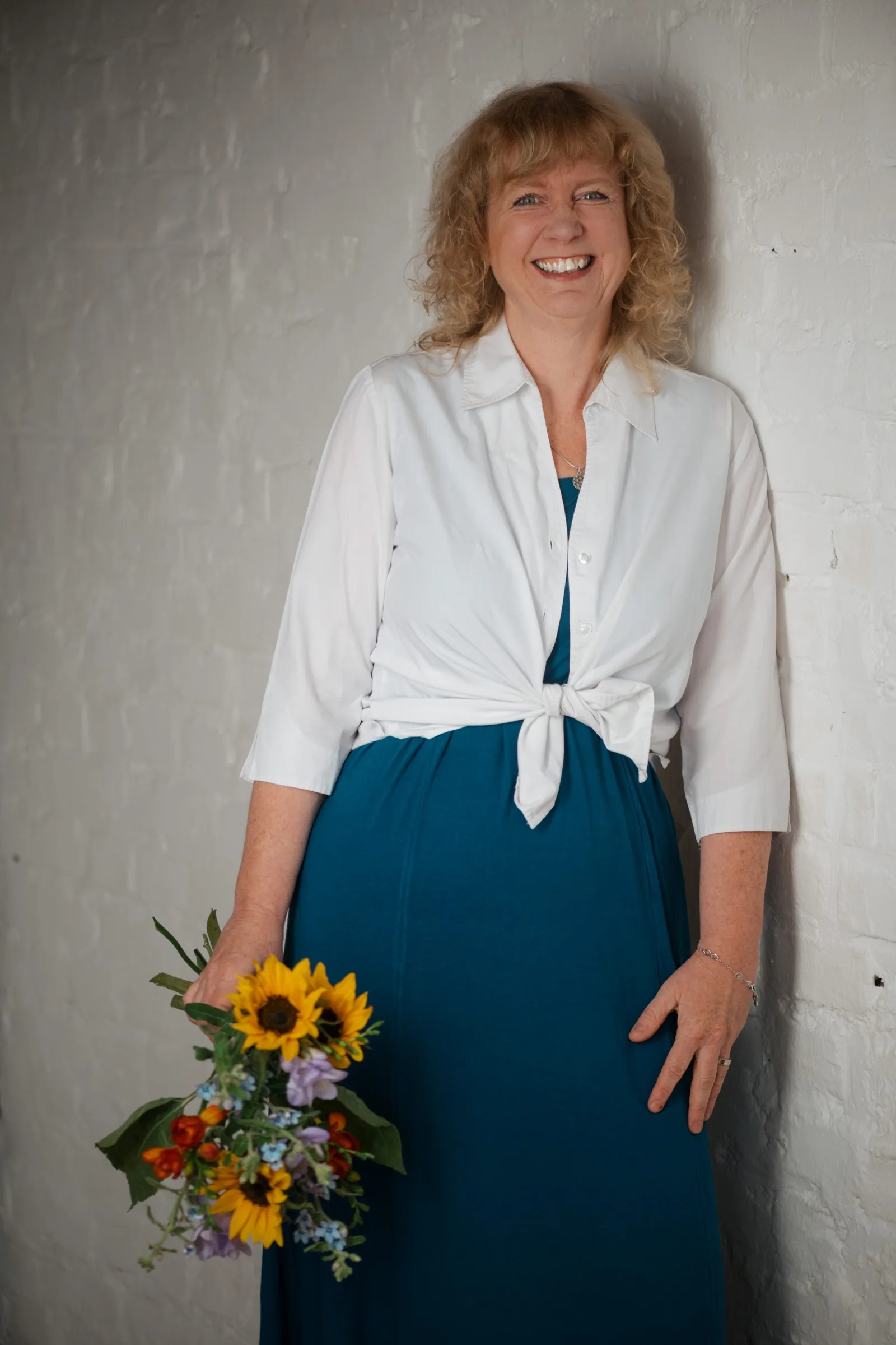 Porträtfoto von Marion Ridder, weiße Bluse mit Schleife, dunkler Rock, Blumenstrauß haltend