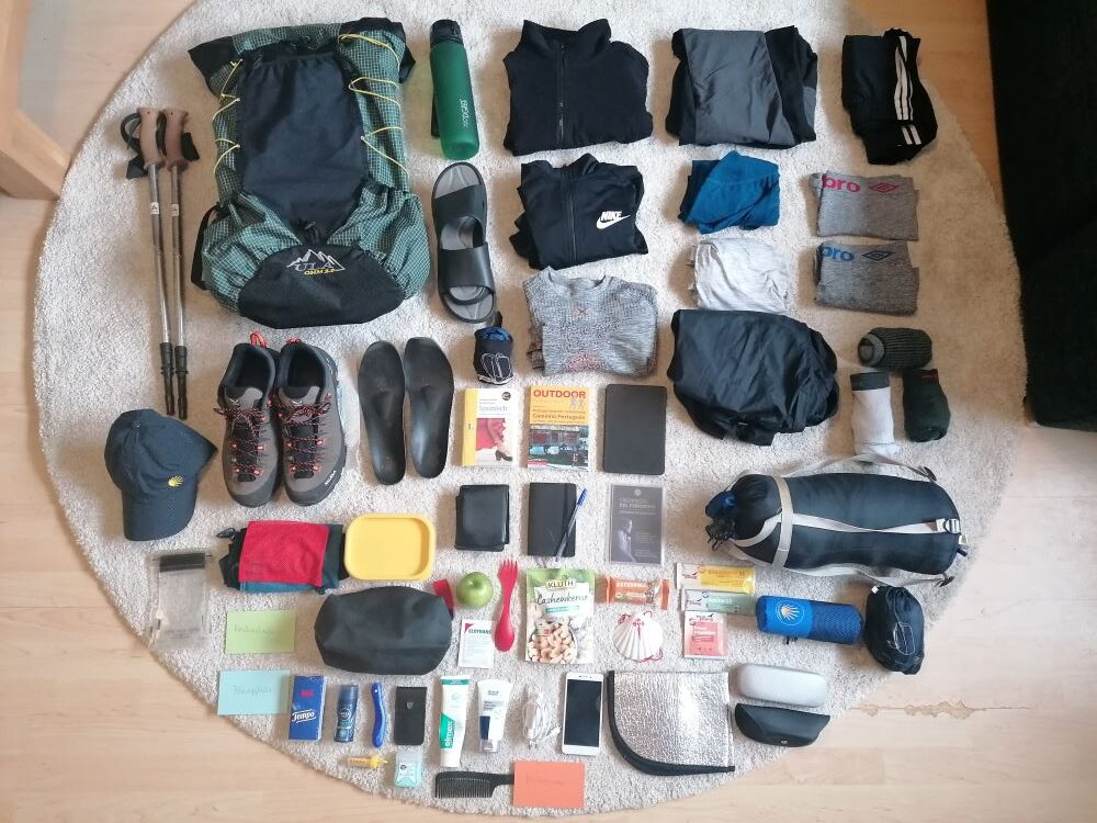 Jakobsweg Packliste mit Rucksack, Wanderschuhen, Kleidung und Ausrüstung ordentlich arrangiert
