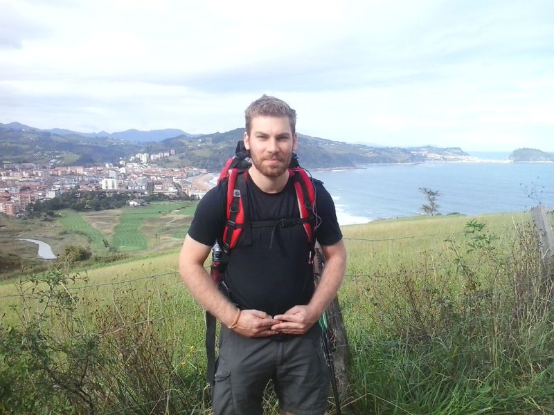 Christoph Erkens mit Rucksack vor Küstenlandschaft und Zarautz