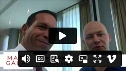 Play-Button auf Video-Thumbnail mit zwei Männern in dunkler Kleidung vor Fenster