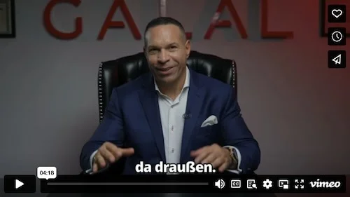 Marc Galal spricht in Video-Interview, trägt dunkelblaues Blazer und weißes Hemd, sitzt auf schwarzem Stuhl vor rotem Hinterg