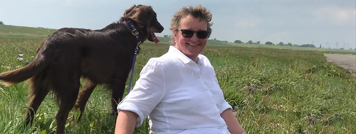 Frau mit Hund an Leine auf Feldweg in Sommerlandschaft