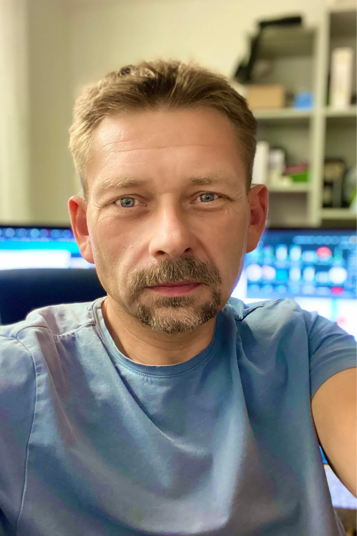 Portrait eines Mannes mit Bart im blauen T-Shirt vor Computer-Setup in einem Büro
