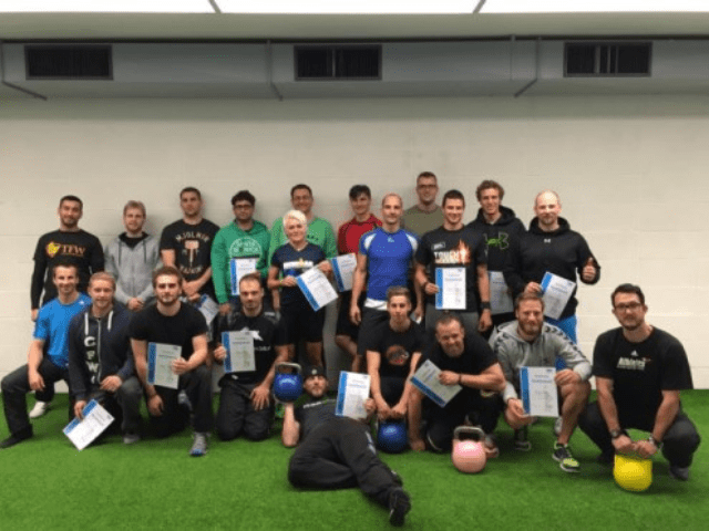 Gruppe von etwa 22 Personen mit verschiedenfarbigen Kettlebells, Zertifikate in Händen