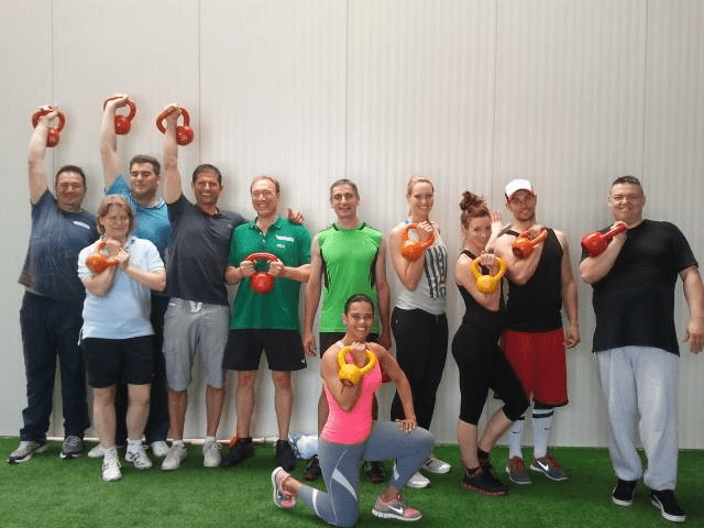 Zehn Personen mit roten und orangenen Kettlebells in den Händen, Gruppenfoto