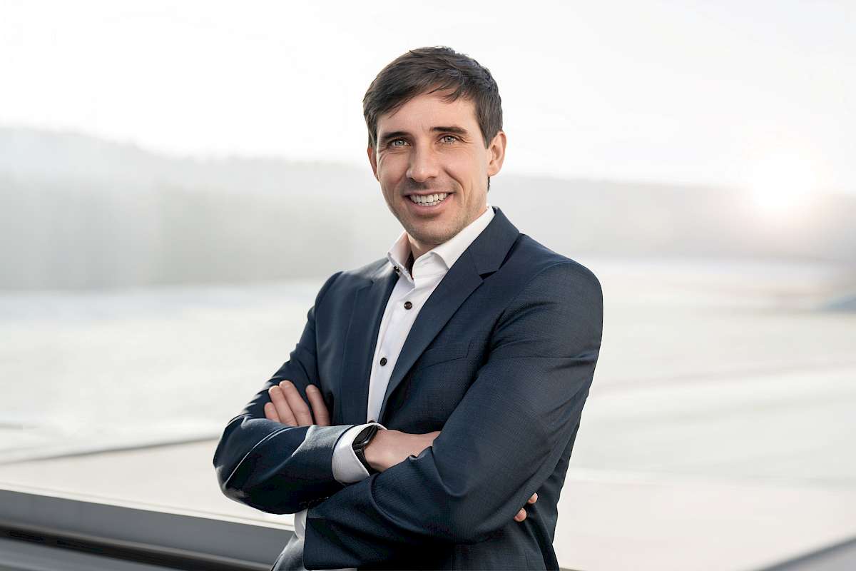 Portrait Andreas Günzel mit verschränkten Armen vor Fenster und Landschaftskulisse