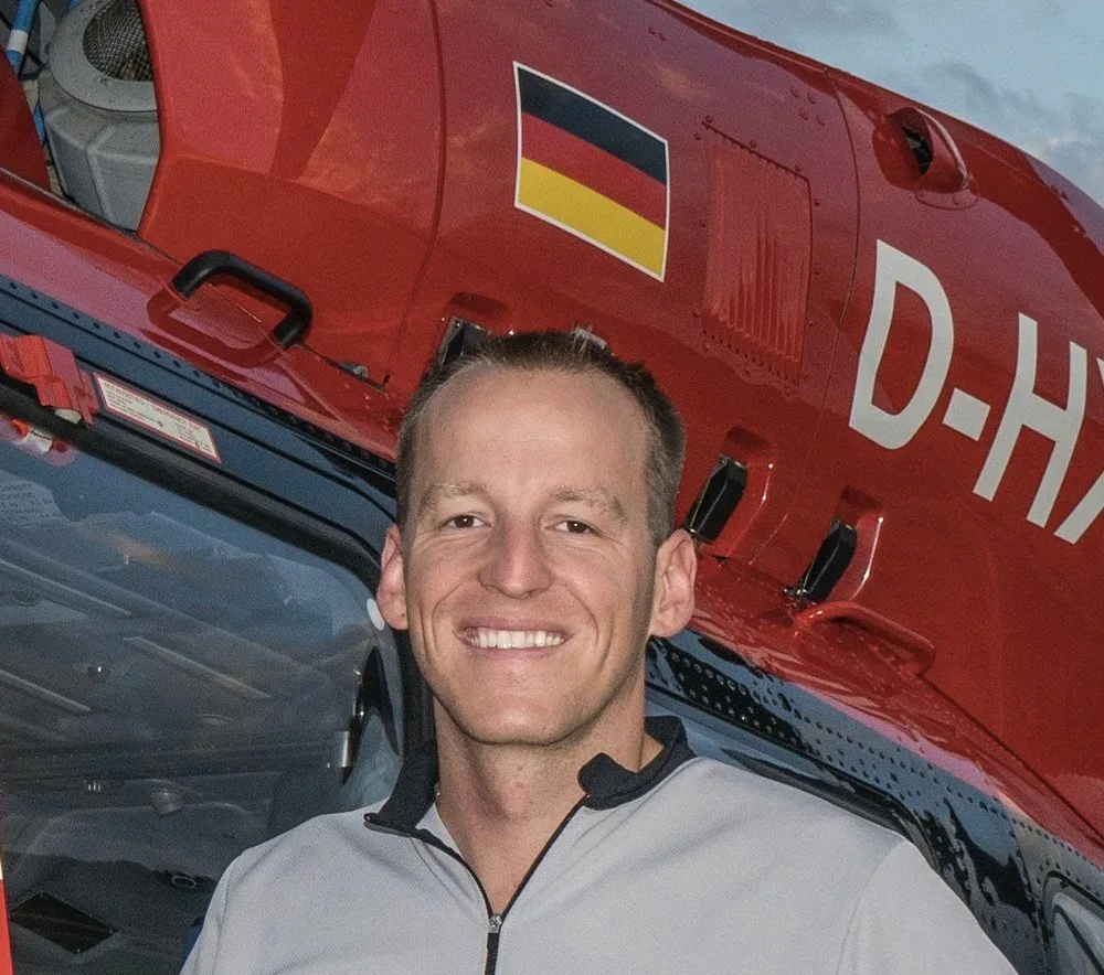 Lucas Sälzle, Notfallsanitäter, lächelnd vor rotem Rettungshubschrauber mit deutscher Flagge