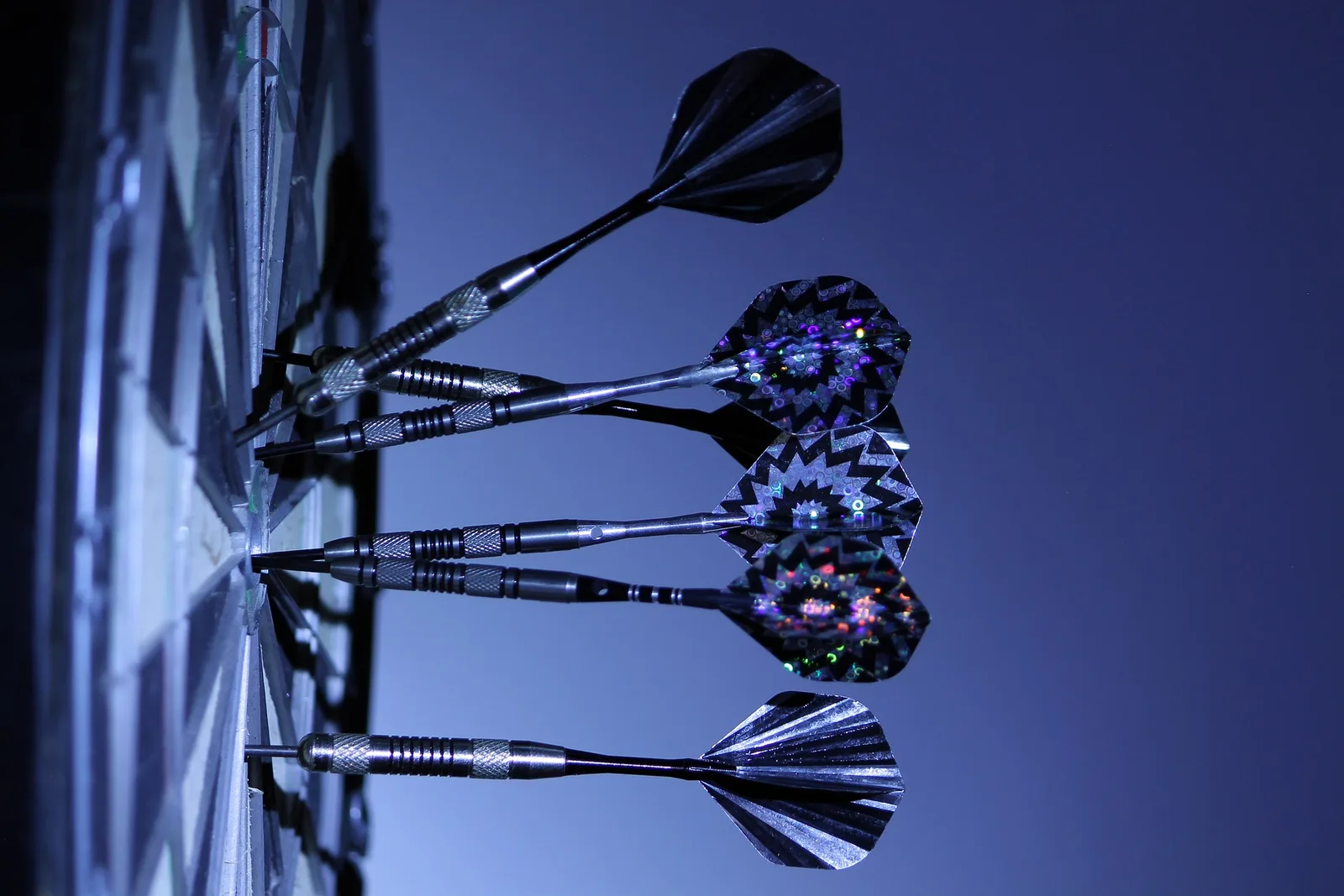 Mehrere Dartpfeile mit bunten Federn vor blauem Hintergrund, zum Dartboard gerichtet