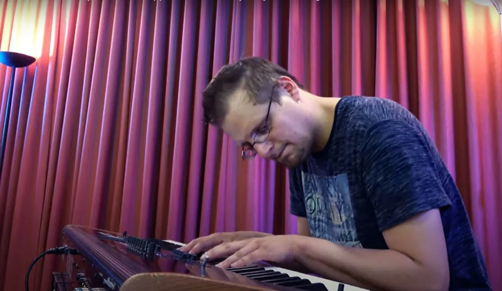 Mann mit Kopfhörern spielt Synthesizer vor rosa-roter LED-Beleuchtung im Recording Studio