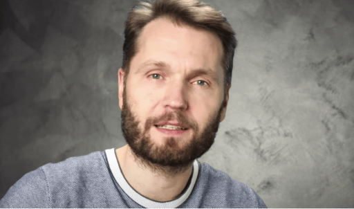 Mann mit Bart in grauem Shirt vor strukturiertem Hintergrund