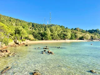 Bottle Beach mit türkisem Wasser, grünen Hügeln und Schnorchlern