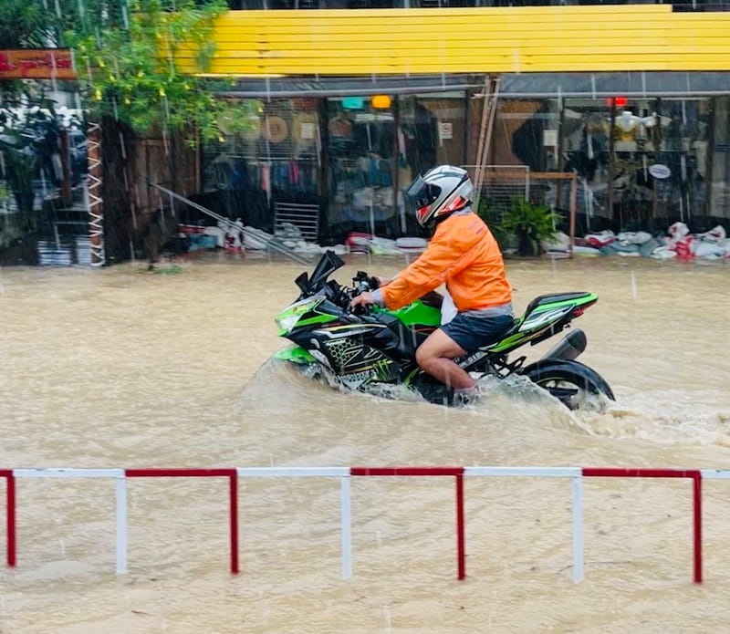 Motorradfahrer in Orange auf grünem Motorrad durch Hochwasser bei Regen
