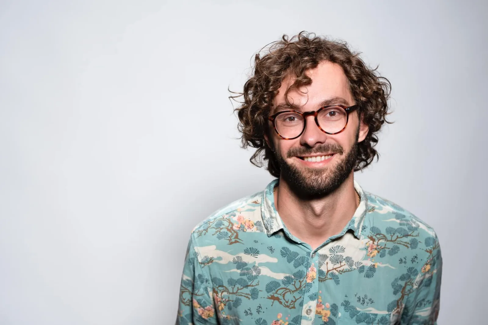 Mann mit Brille in gemustertem Hemd vor grauem Hintergrund