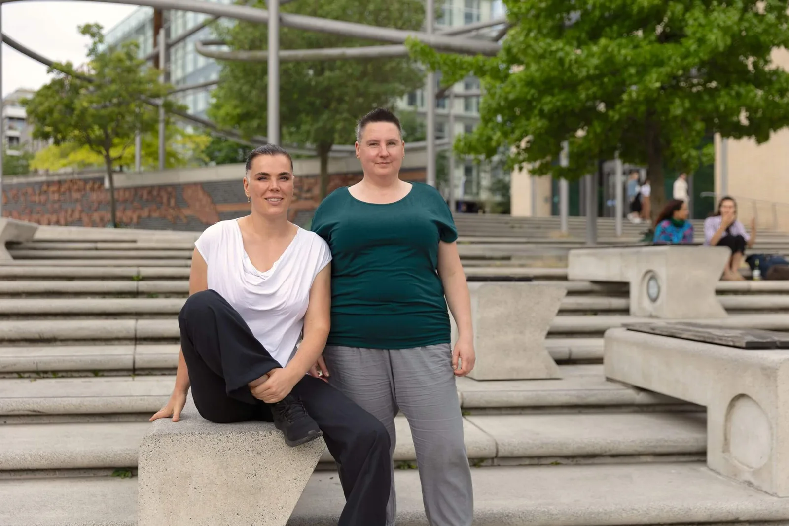 Zwei Frauen posieren auf breiten Betonstufen in urbaner Parkanlage