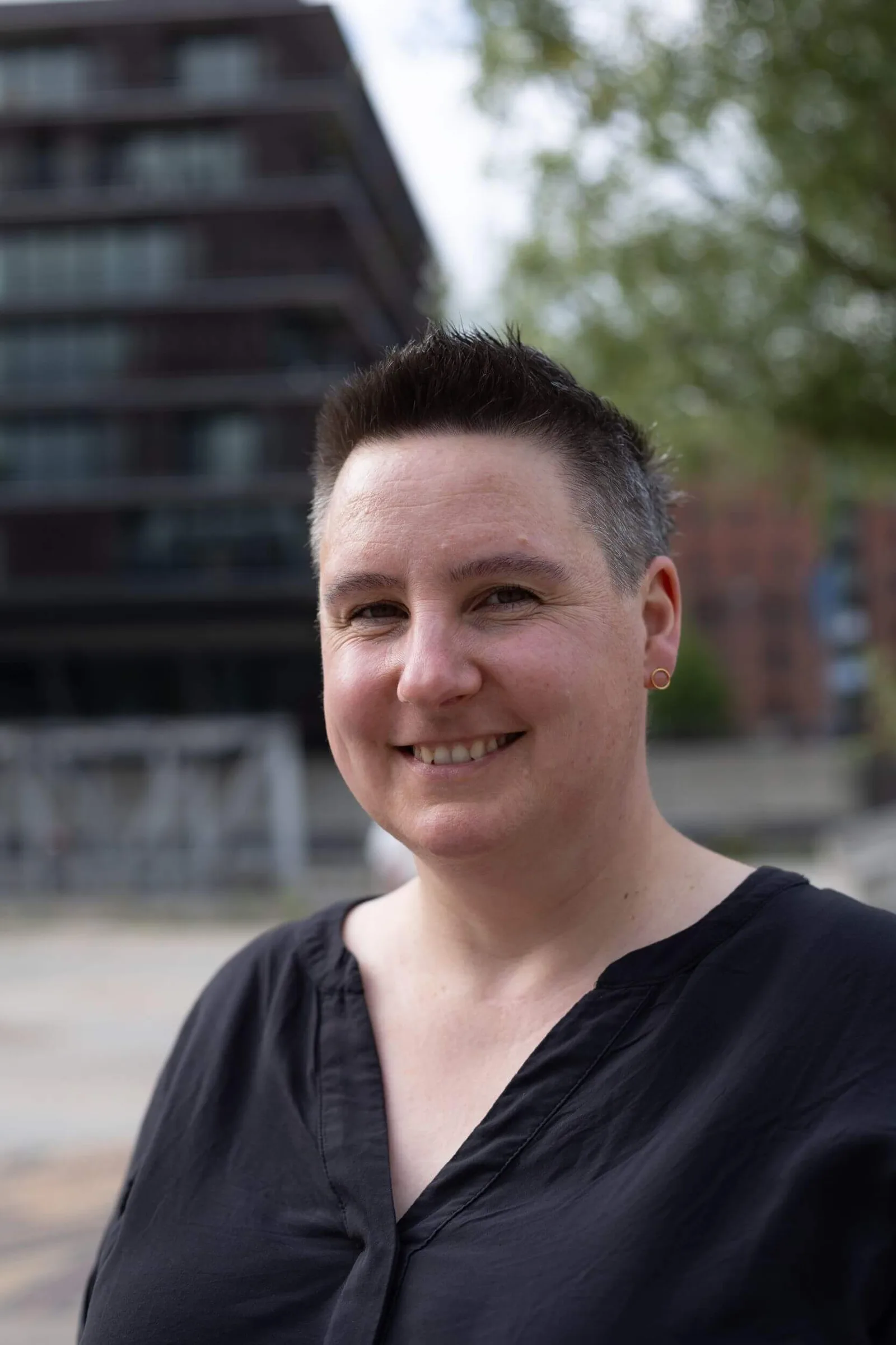 Porträt von Frau mit kurzen dunklen Haaren und Ohrring vor Urban-Hintergrund