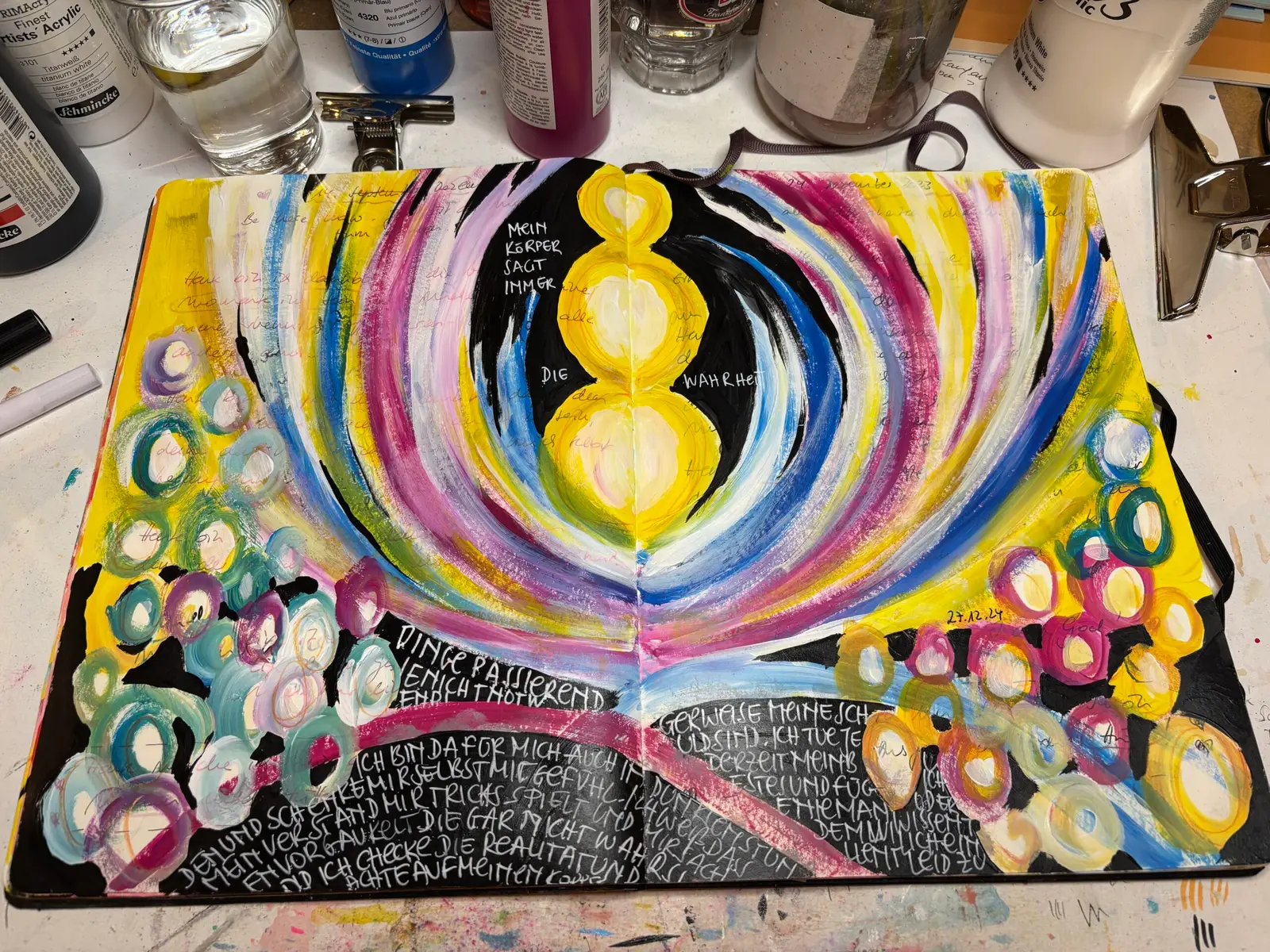 Offenes Mixed-Media-Kunstbuch mit bunten konzentrischen Kreisen, gelben Kugeln und handgeschriebenem Text auf schwarzem Hinte