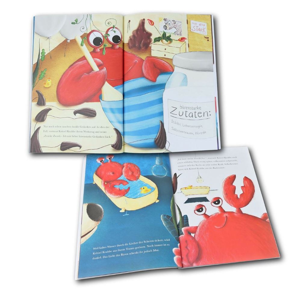 Aufgeschlagenes Kinderbuch Kritzel Krabbe mit Illustrationen einer roten Krabbe, Badeszenen und Affirmationskarten