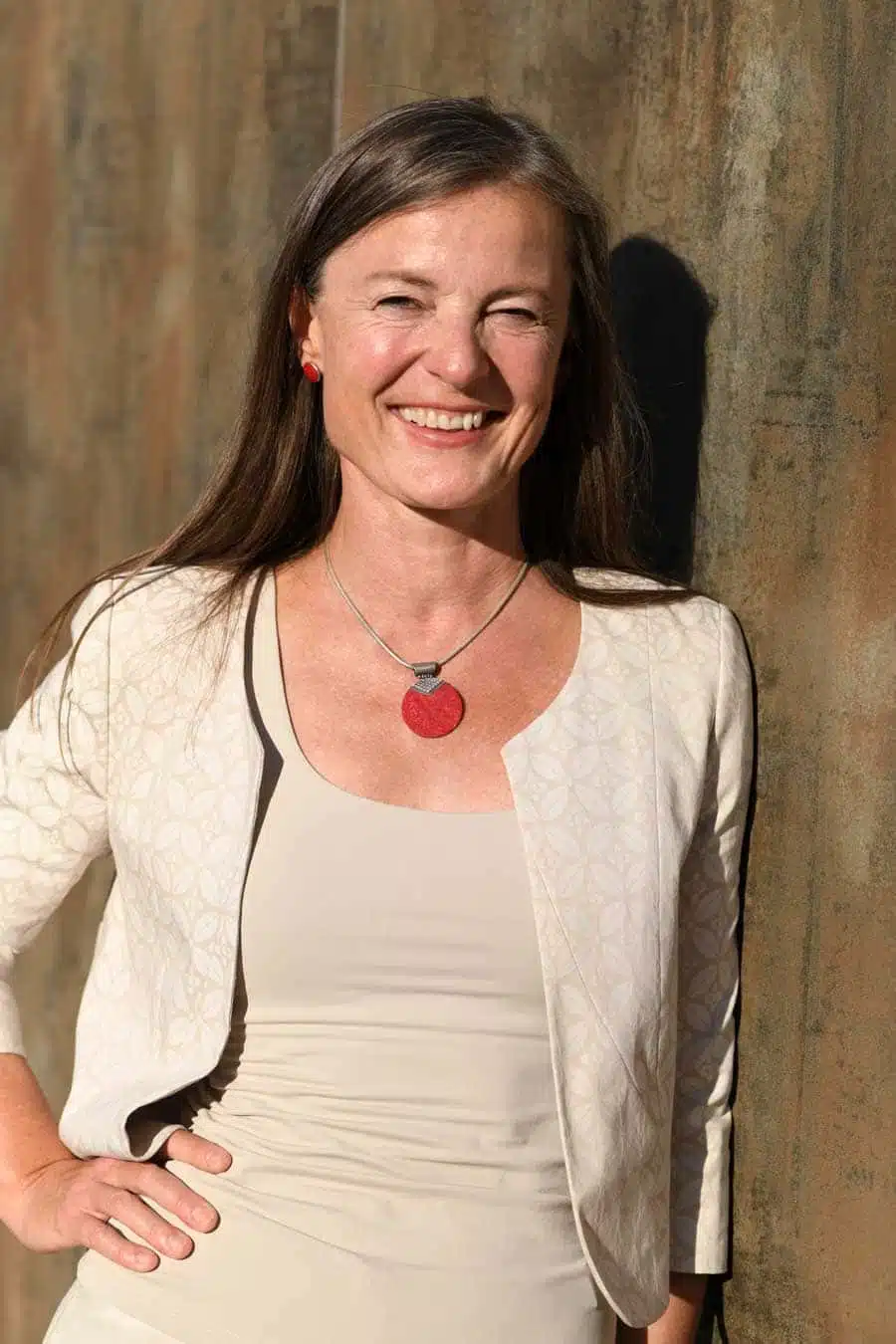 Frau mit langen dunklen Haaren, roten Ohrringen und rotem Herz-Anhänger, cremefarbener Blazer