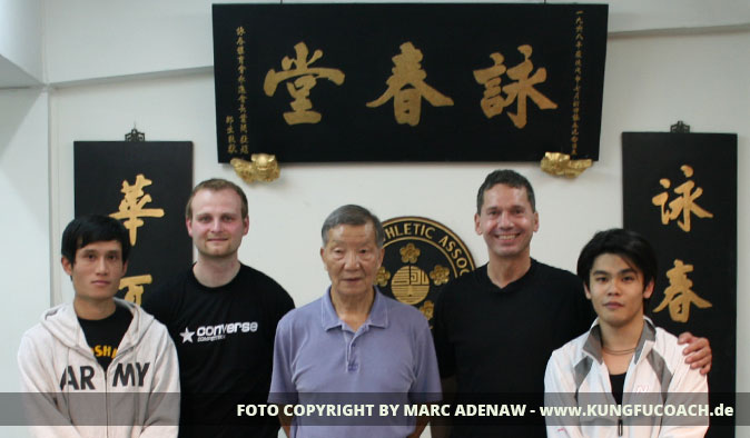 Fünf Personen vor asiatischer Wanddekoration mit goldenem Text und Wappen, Gruppenfoto aus Kung-Fu-Schule