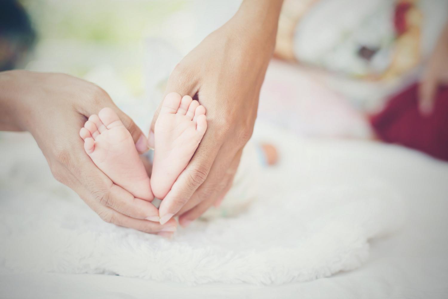 Babyfüße in erwachsenen Händen bei Babymassage, zartes Handling auf weißem Untergrund