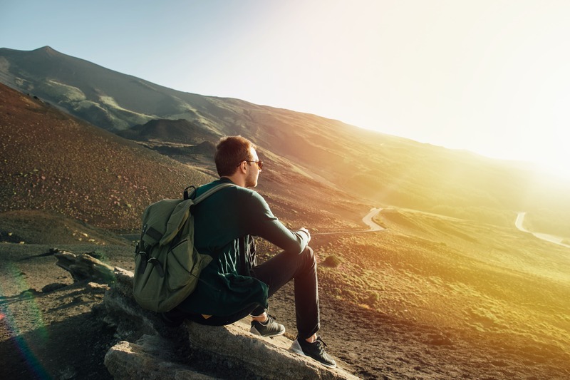 Mann mit Rucksack sitzt auf Bergkuppe im Sonnenaufgang