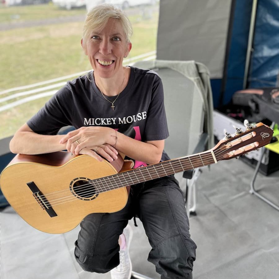 Sylvia Weber hält Akustikgitarre lächelnd im Bus sitzend