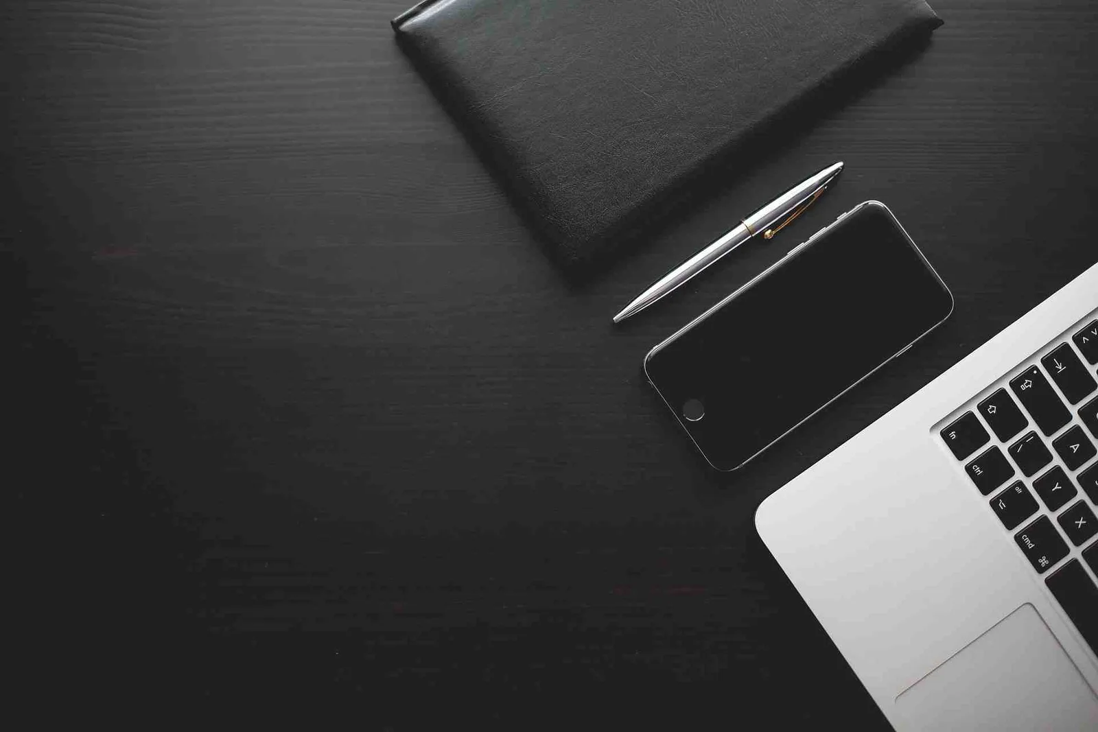 Schreibtisch von oben mit Laptop, Smartphone, Stift und schwarzem Notizbuch