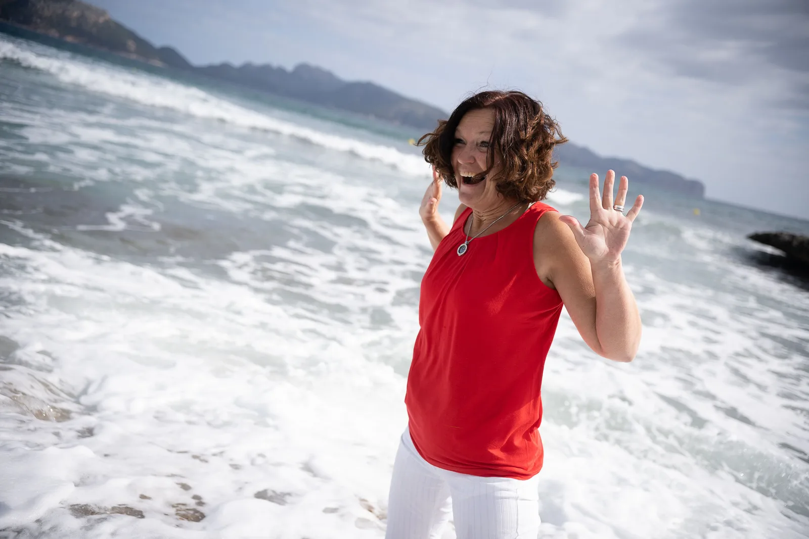 Frau in rotem Top am Strand mit Wellen im Hintergrund