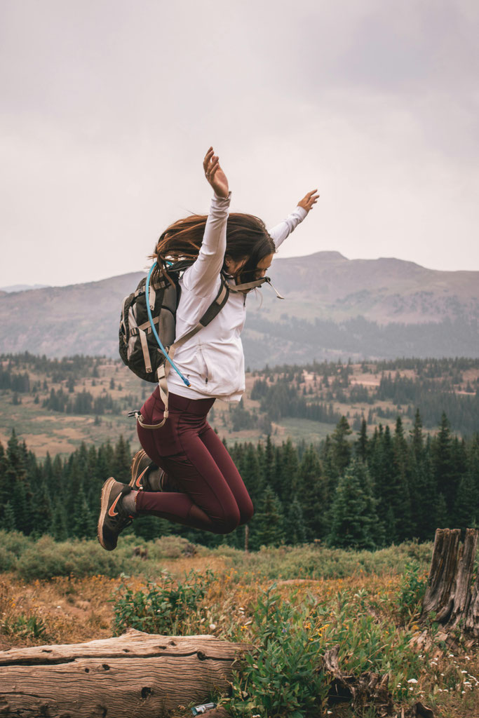 Frau springt jubelnd in Berglandschaft mit Rucksack