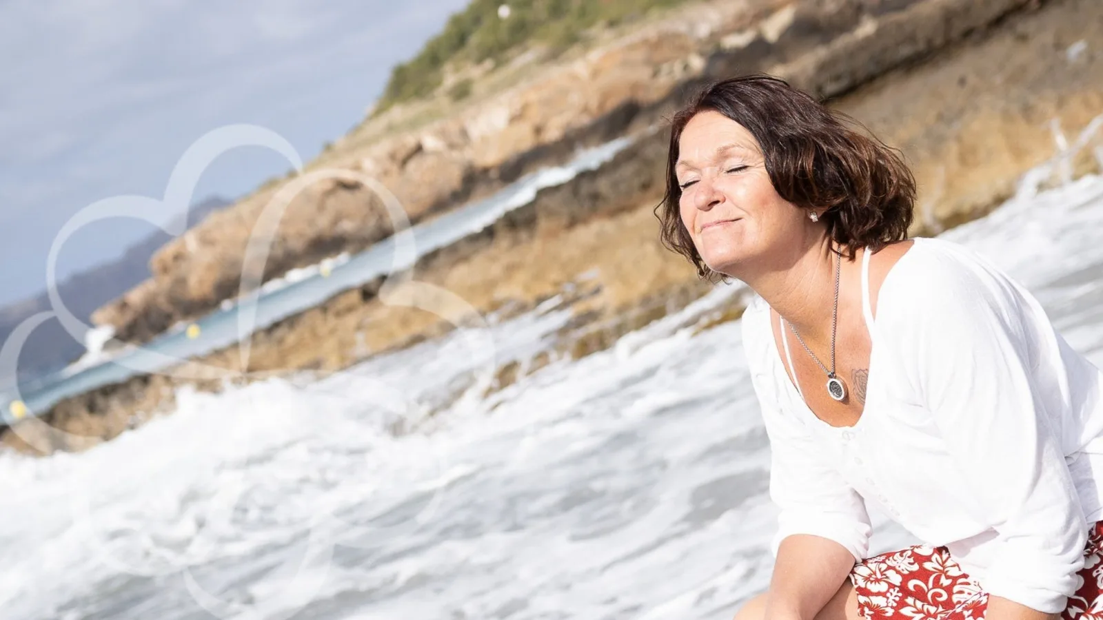 Frau sitzt entspannt am Strand mit Bergen im Hintergrund