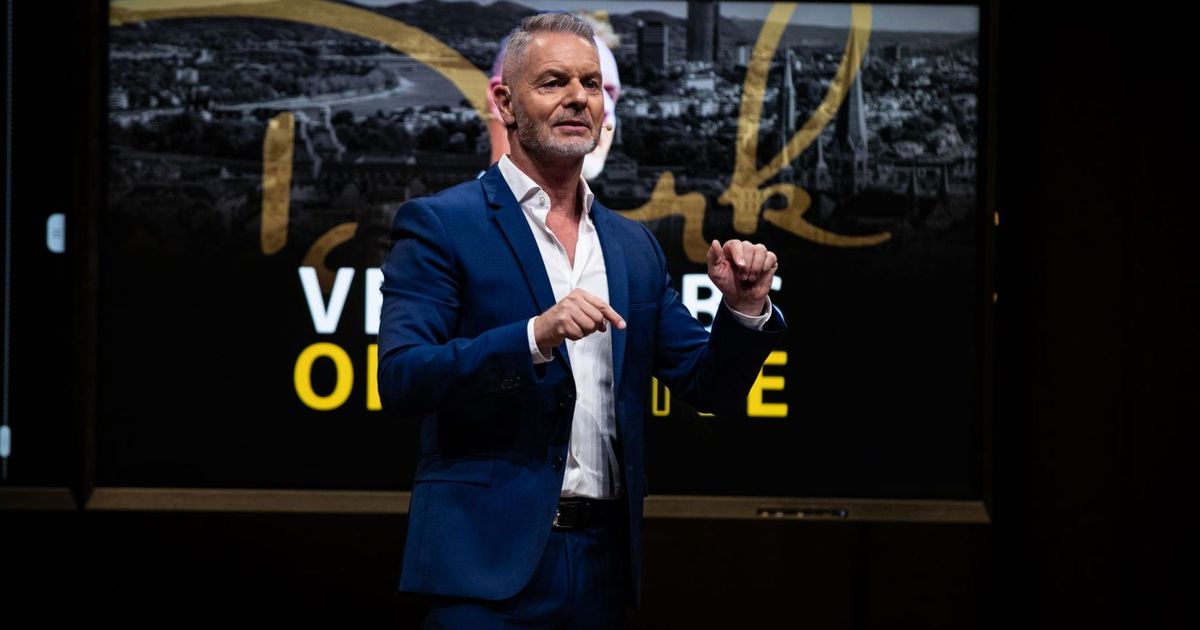 Dirk Kreuter auf der Bühne im blauen Anzug, sprechend und gestikulierend vor Stadtkulisse