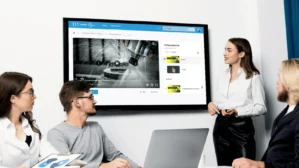 Vier Personen schauen auf Monitor mit Fertigungs­technik-Lernvideo und MyDigiAcademy-Kurs­oberfläche