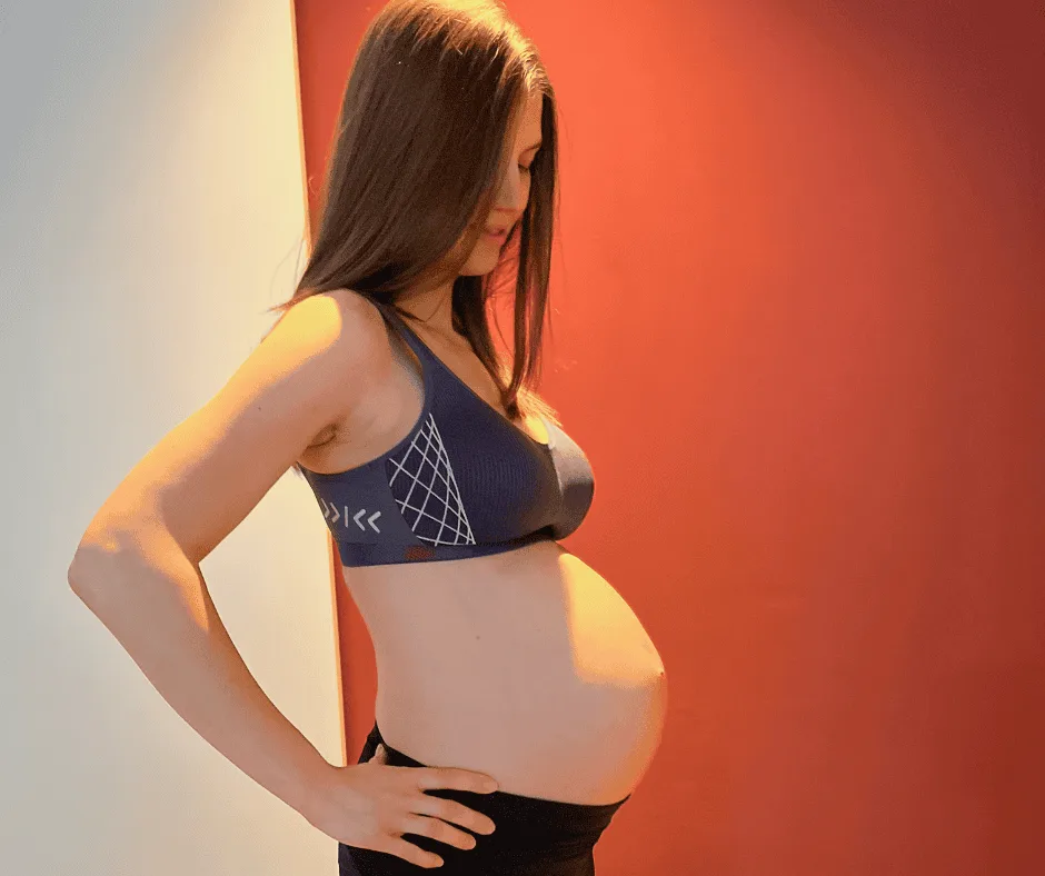 Let's get Moving – Fitnesskurs für Schwangere von Birte Glang 7 Schwangere Frau in schwarzem Sportbustier vor rot-gelbem Hintergrund