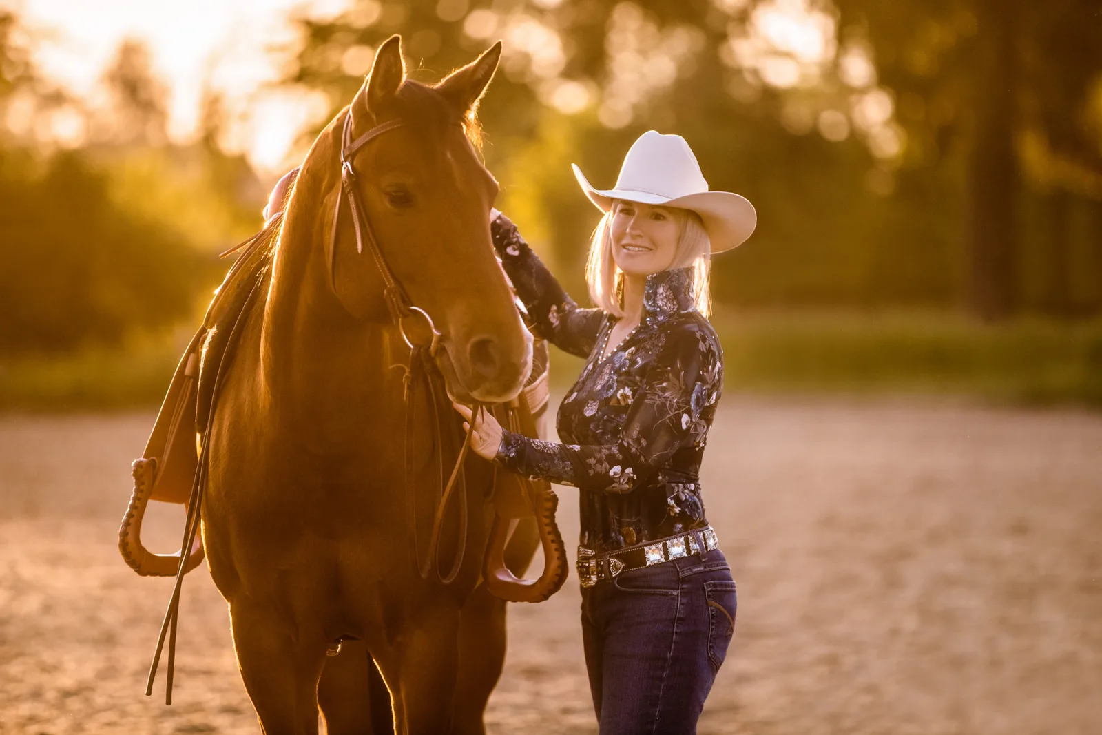 Blonde Frau mit weißem Cowboyhut streichelt braunes Pferd, Ganzkörperaufnahme, Außenbereich