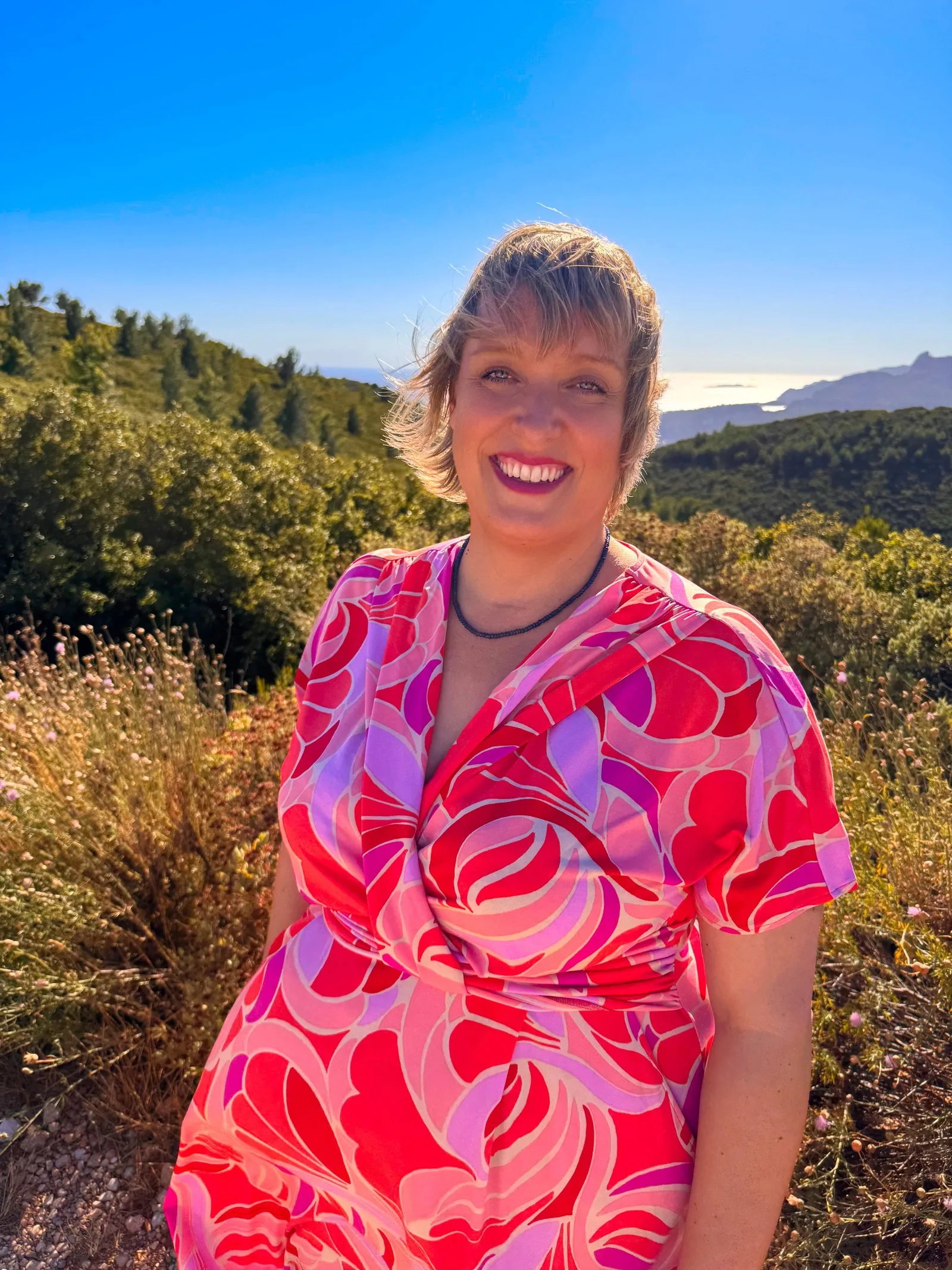 Portrait von Britta Kunst lächelnd in farbenfrohem Kleid in Naturlandschaft