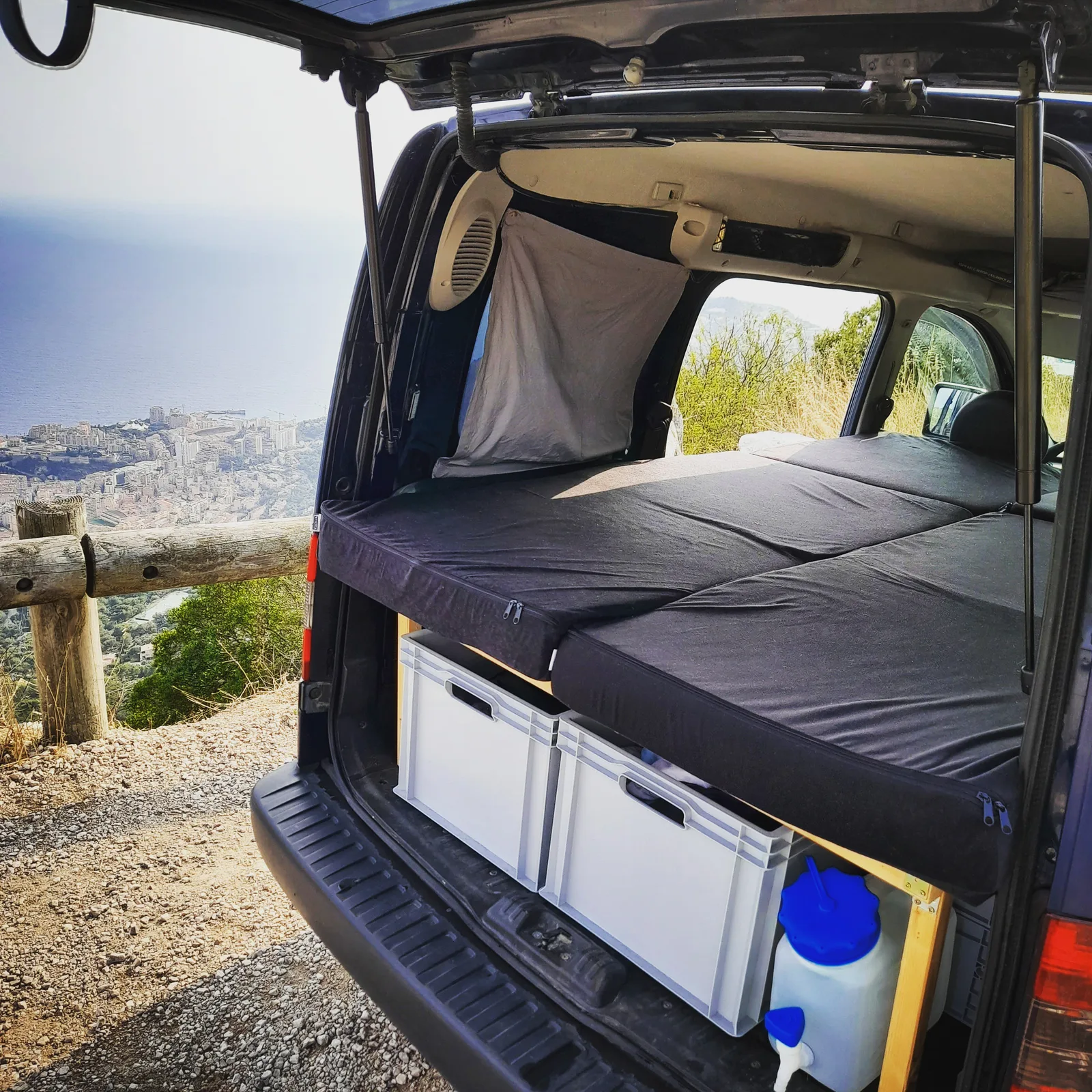 Ford Tourneo Courier mit ausgeklapptem Doppelbett, Matratze und Stauraum mit Behältern, Berglandschaft im Hintergrund