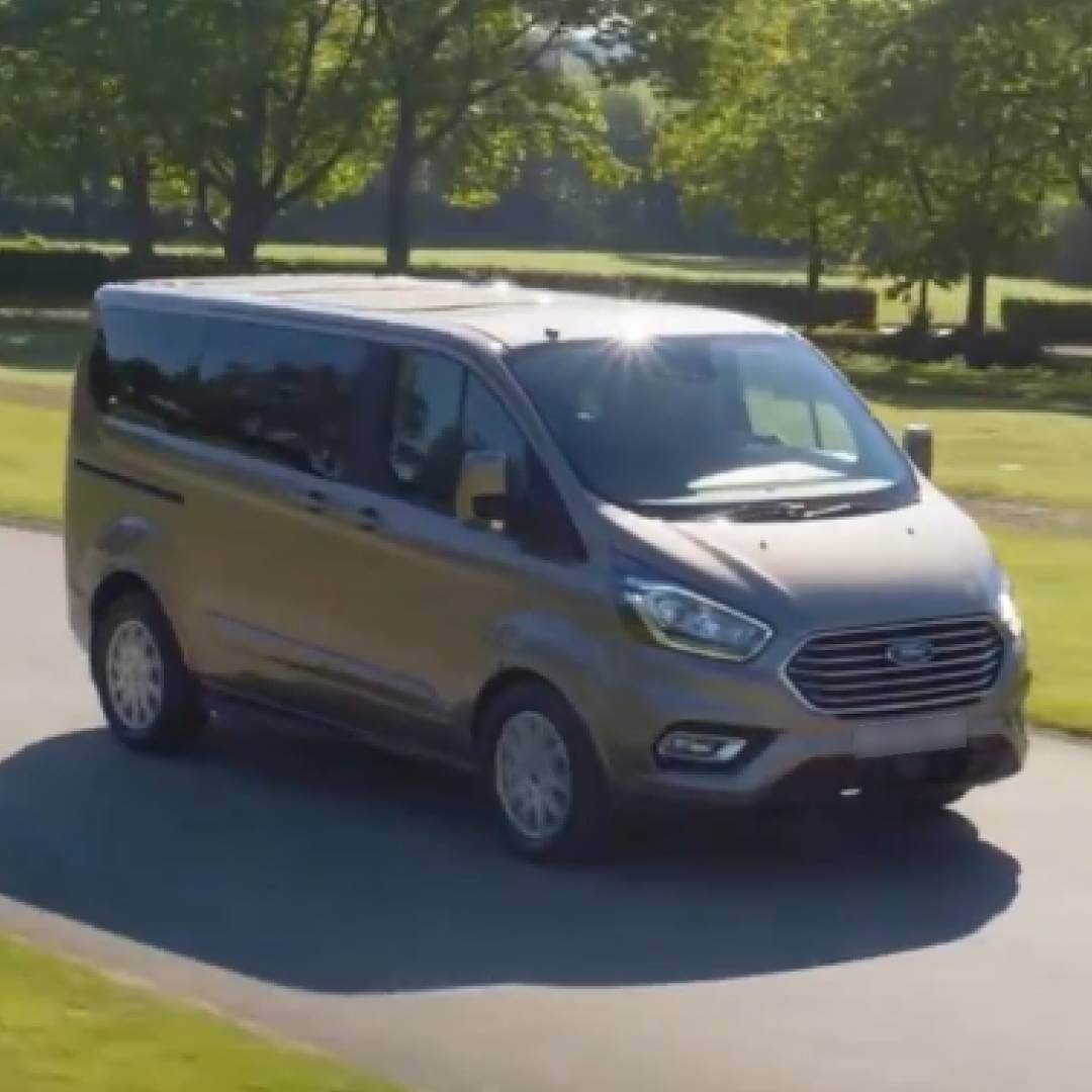 Ford Tourneo Custom Kombi-Van in beige-grau auf Parkplatz mit Bäumen