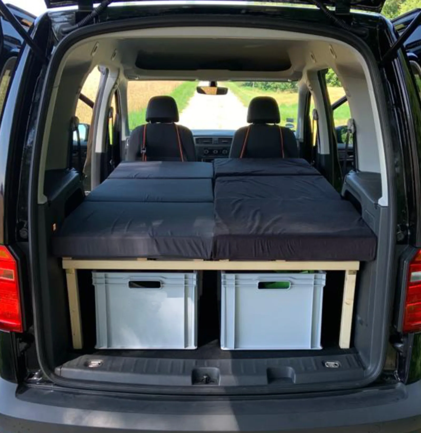 VW Caddy Doppelbett mit schwarzer Matratze und weißen Aufbewahrungsboxen unter dem Bett