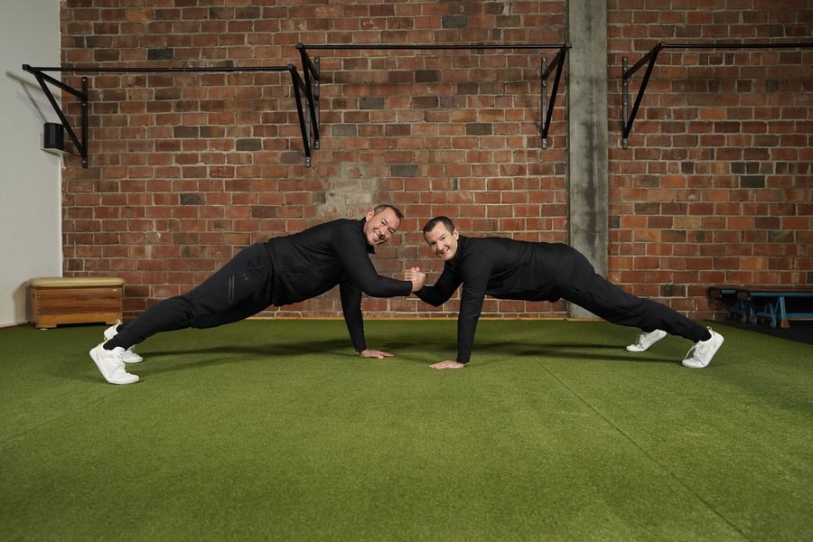 Zwei Männer in schwarzer Sportkleidung führen Liegestütze durch, Level up Krafttraining