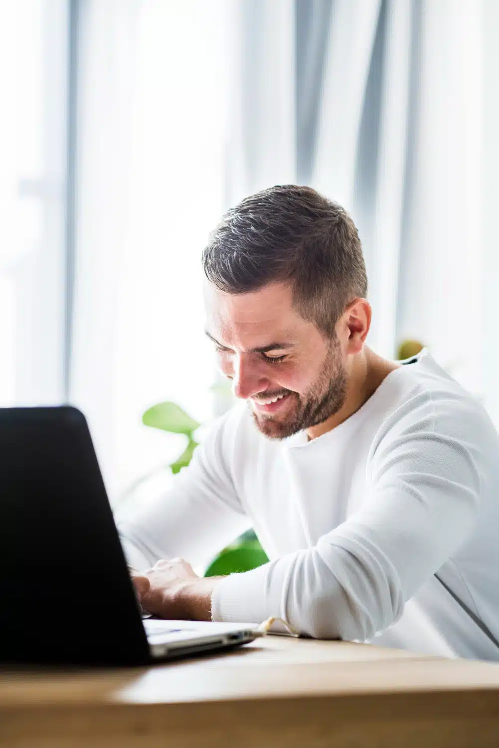 Mann in weißem Hemd arbeitet konzentriert am Laptop am hellen Schreibtisch