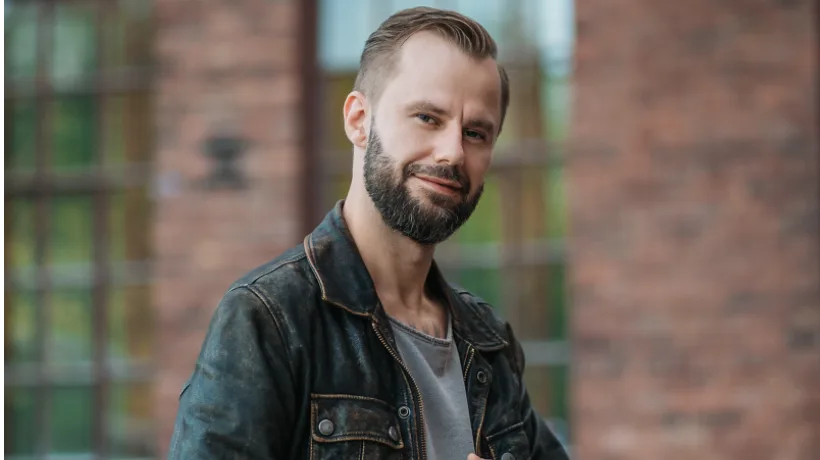 Liebesphrasen – E-Book über Flirtsätze von Darius Kamadeva 3 Headshot von Darius Kamadeva in Jeansjacke vor Backsteingebäude mit fokussiertem Blick