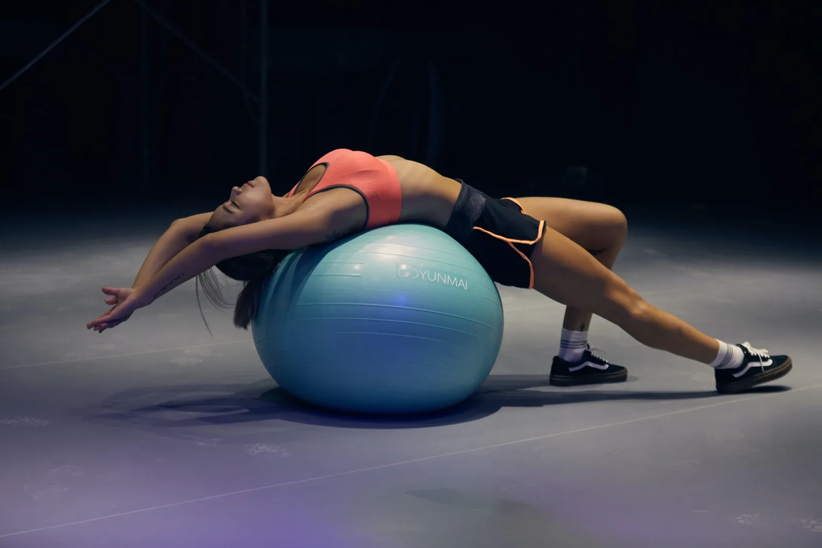 Frau mit Stabilitätsball beim Rückentraining auf dunklem Untergrund