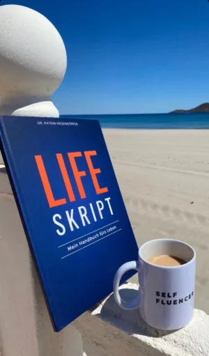 LifeSkript Buch am Meer mit Kaffeetasse und Skulptur