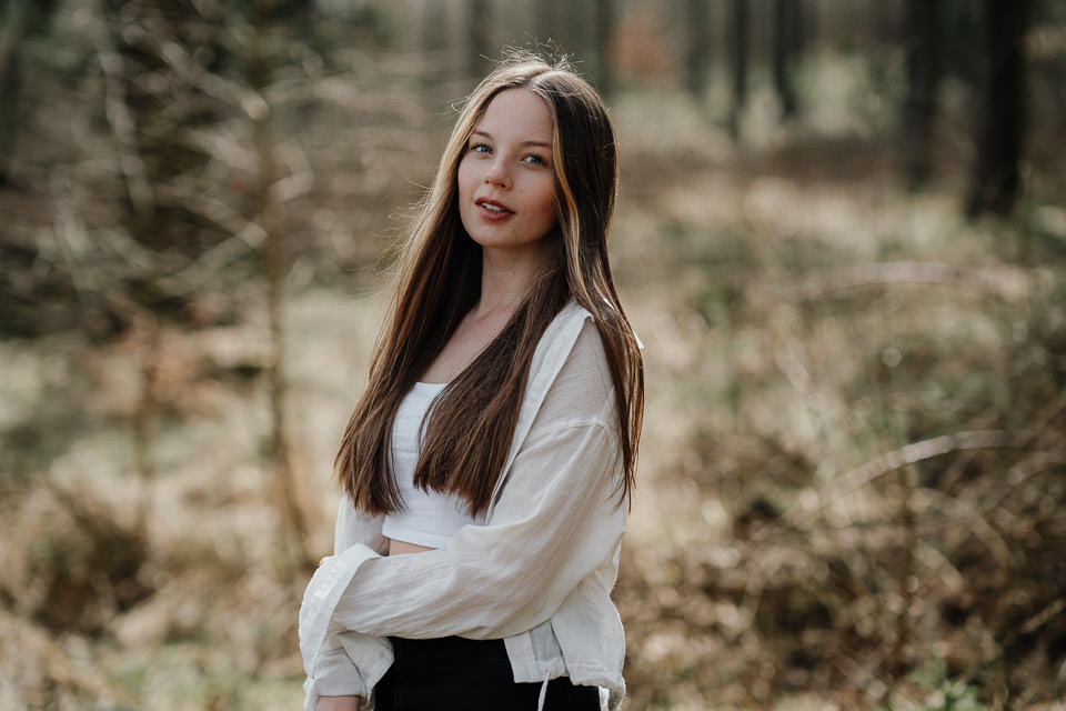 Porträt einer jungen Frau mit langen braunen Haaren im Wald, weiße Bluse