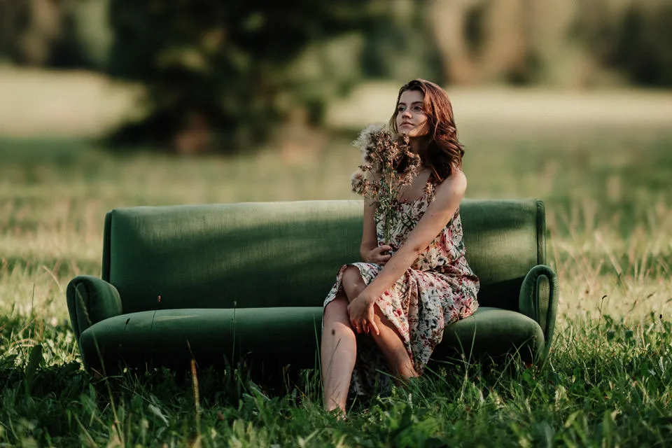 Frau mit braunen Haaren auf grünem Sofa im Grünen, Blumenmuster Kleid